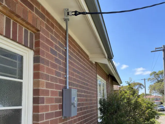 Overhead service cable and point-of-attachment bracket on a brick house exterior in Rose Bay